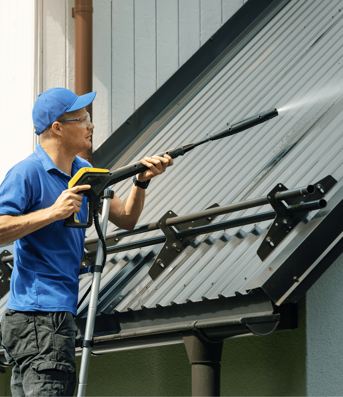Worker using power washer on roof