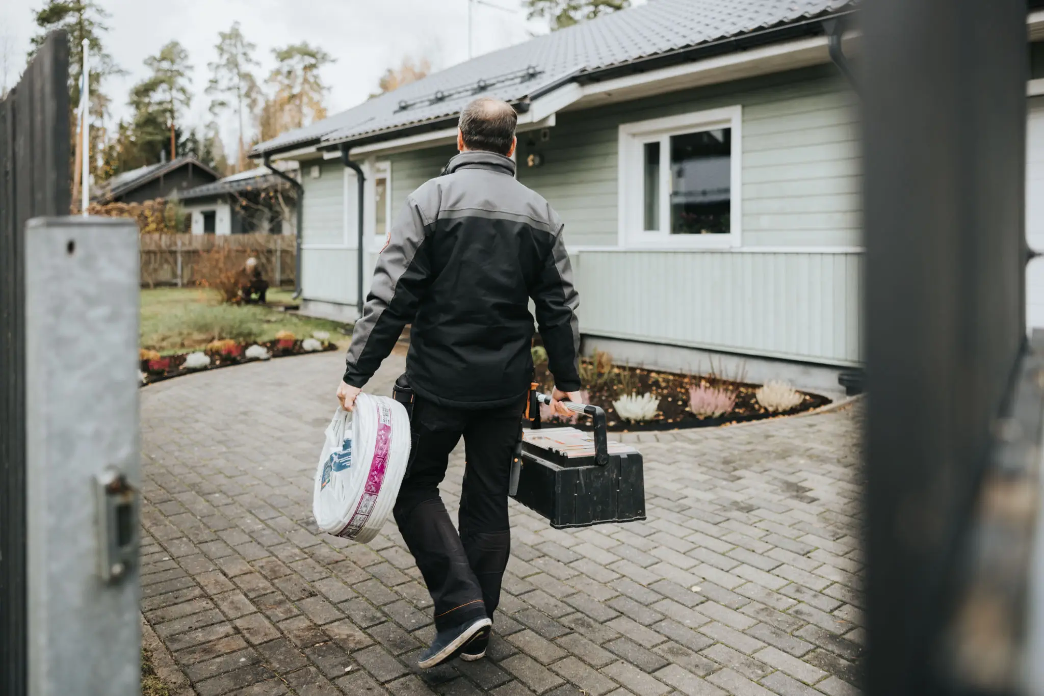 A worker carrying tools and supplies walking to a house.