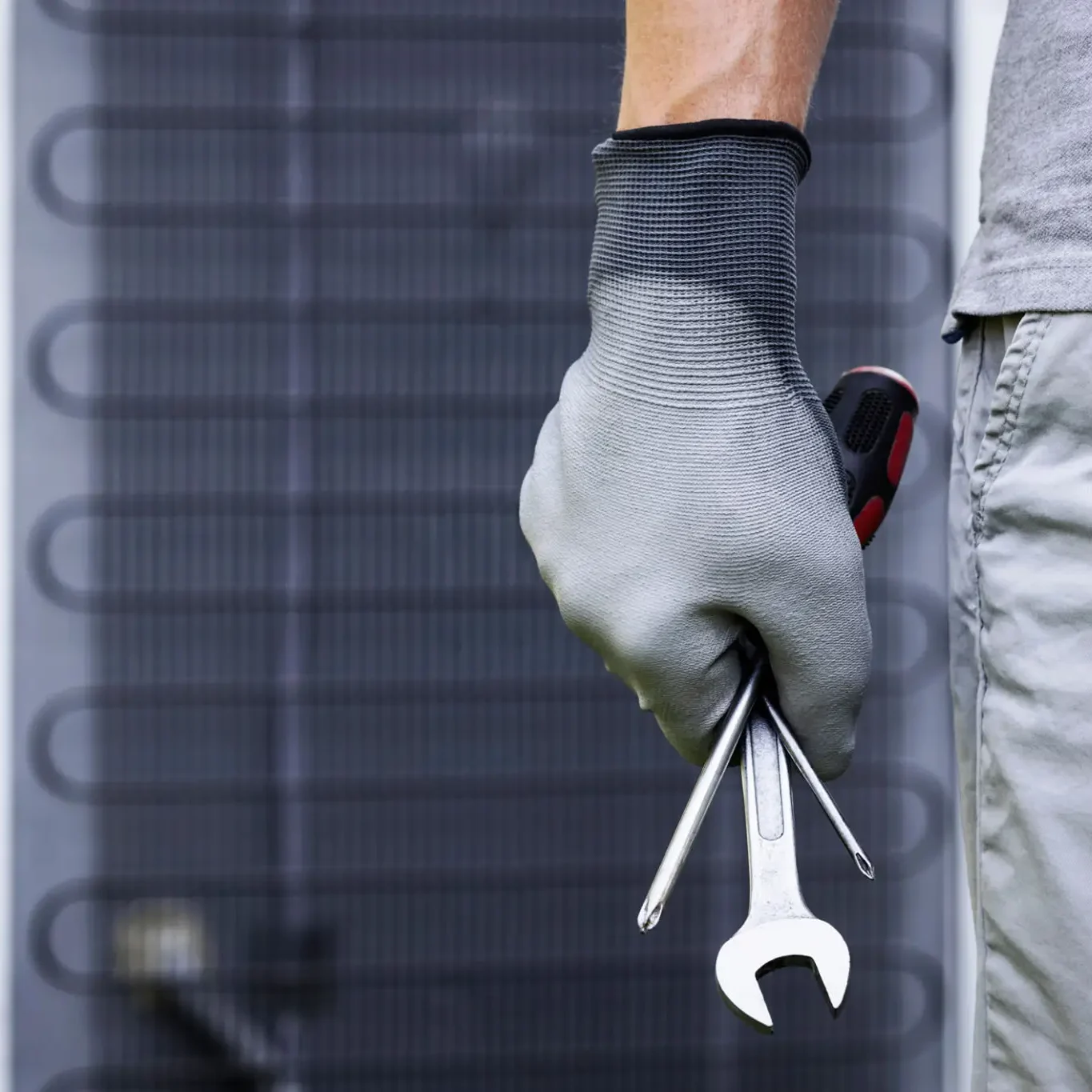A technician holding tools while working on an HVAC unit.
